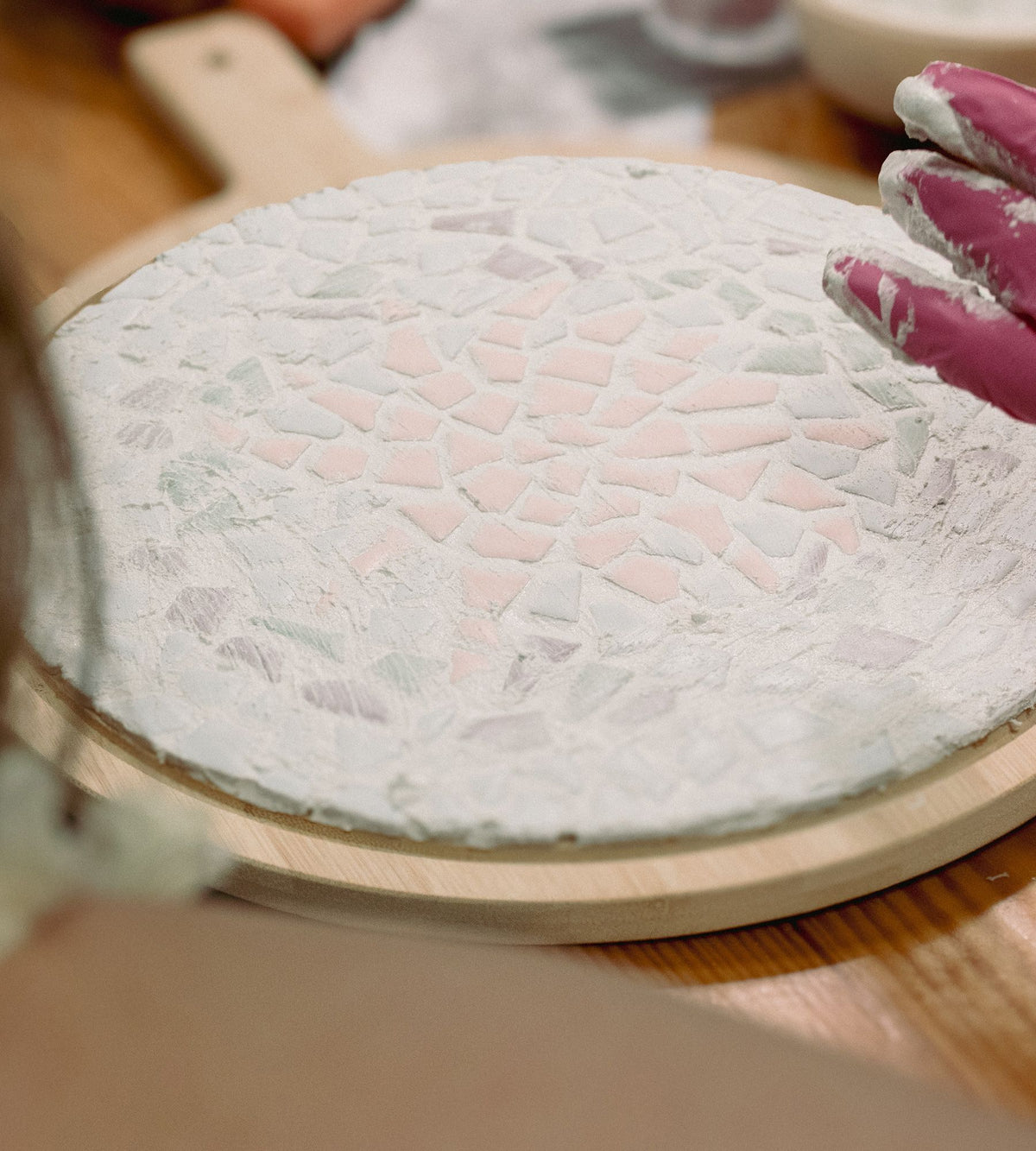 Ein fertiges Mosaik auf einem runden Holzbrett wird verfugt